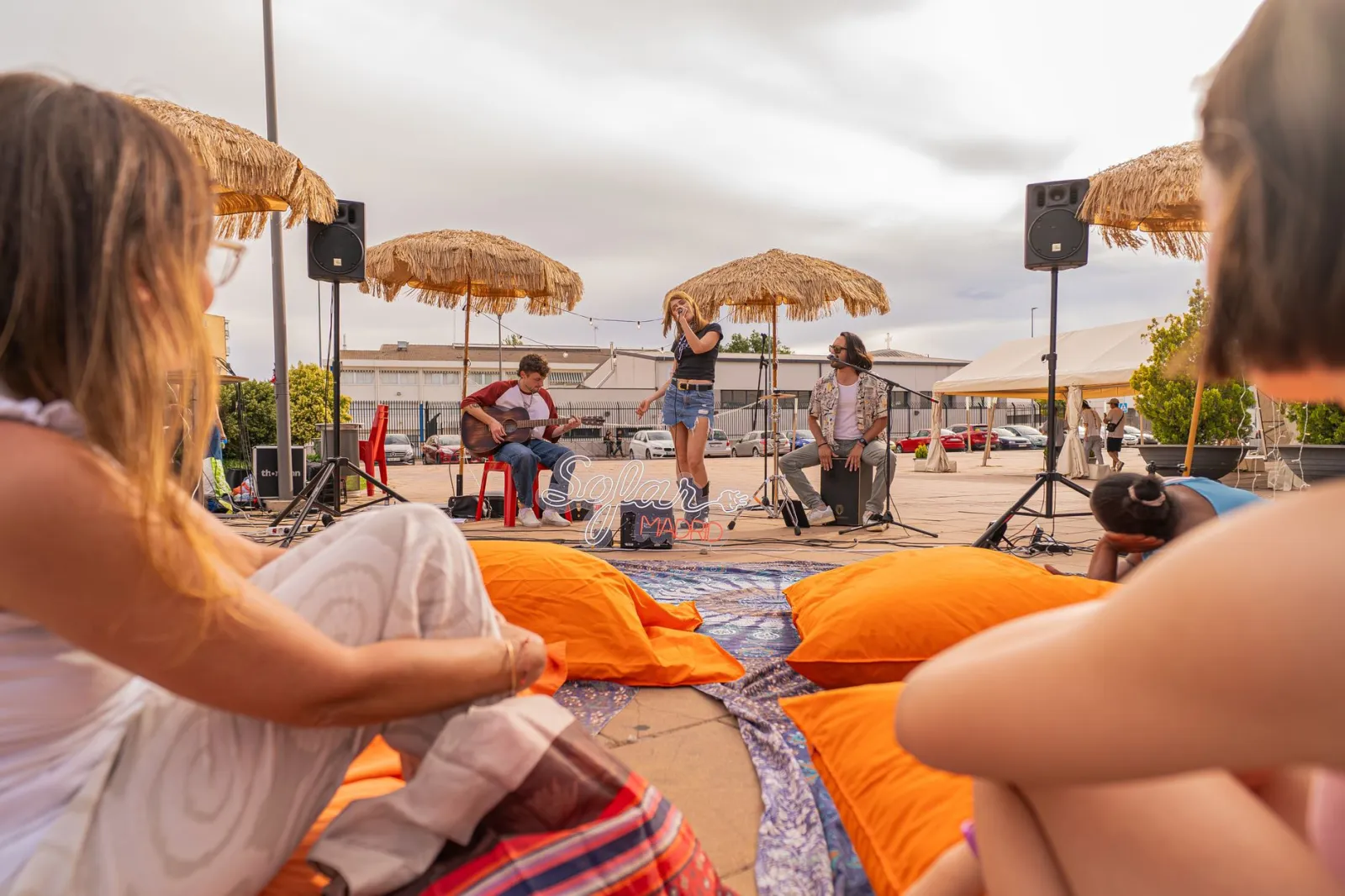 Live music performance outdoors at a festival with audience and straw umbrellas.