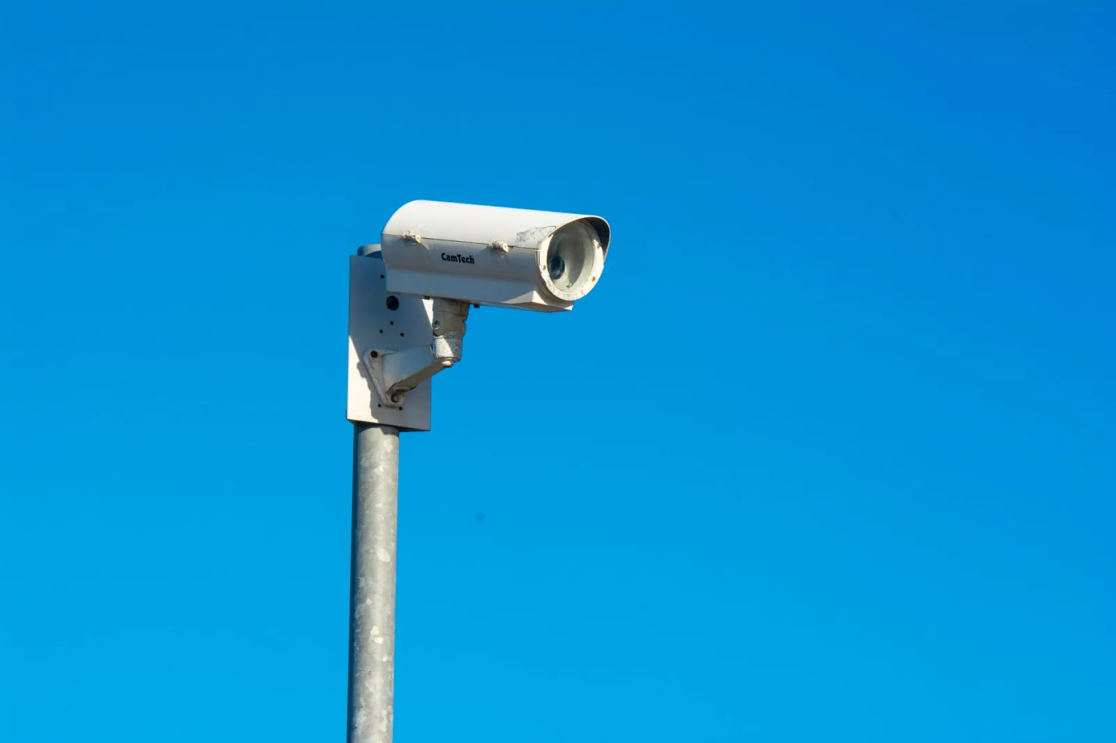 White security camera mounted on a pole under a clear blue sky, symbolizing security and surveillance.