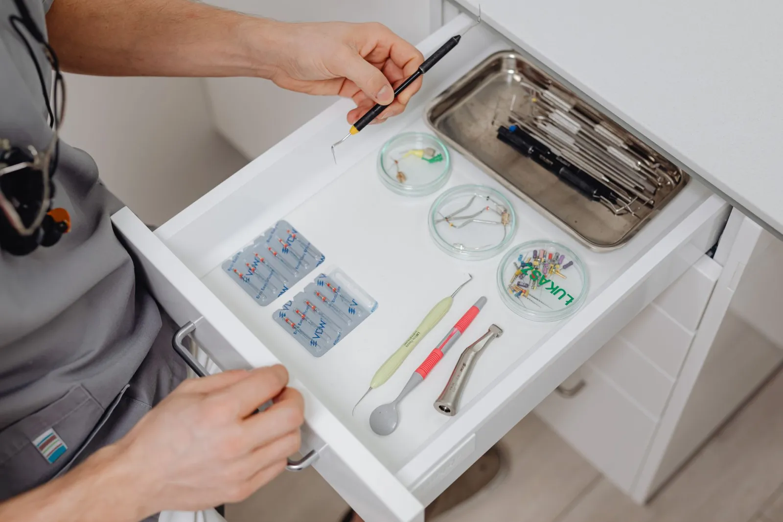 A dentist arranges dental tools in a clinic drawer, showing modern equipment.