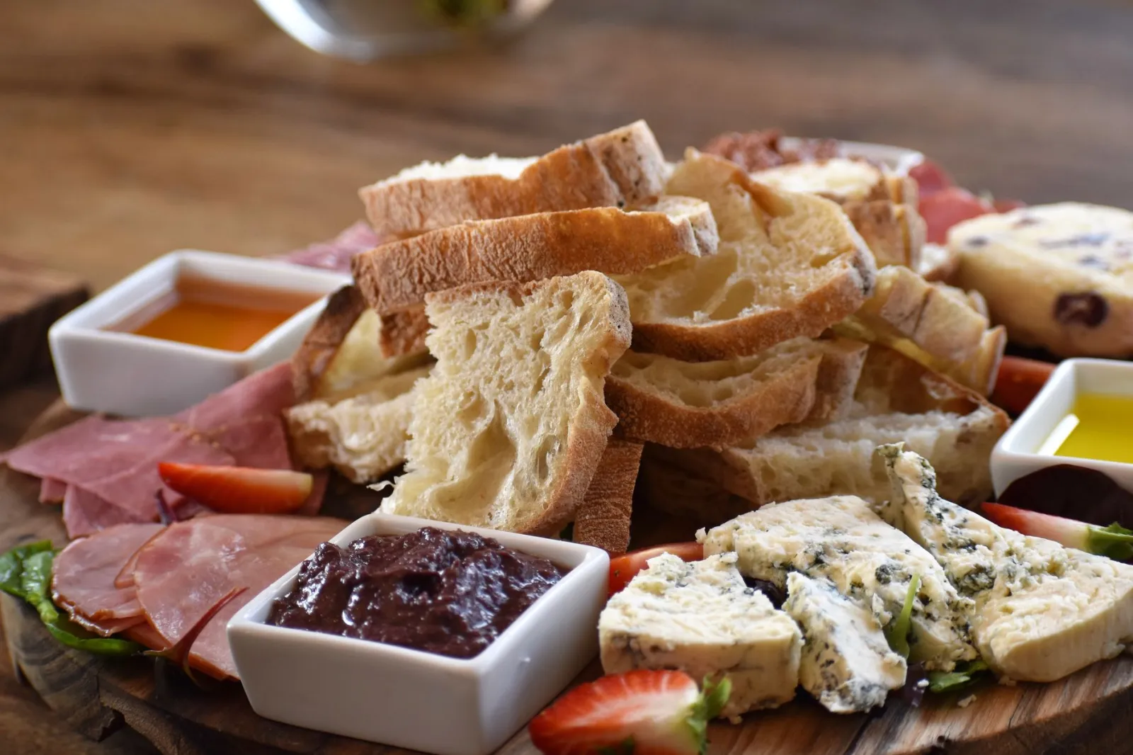 A delightful array of artisan bread, cheese, and ham with jams on a rustic wooden platter.