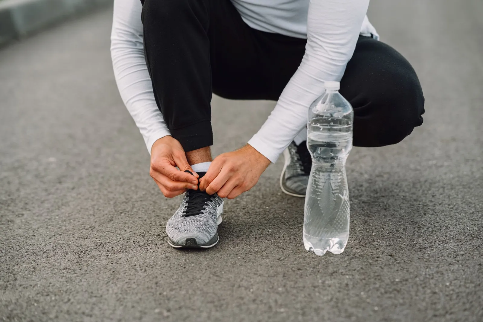 Runner tying shoelaces on the road with a water bottle beside. Fitness preparation.